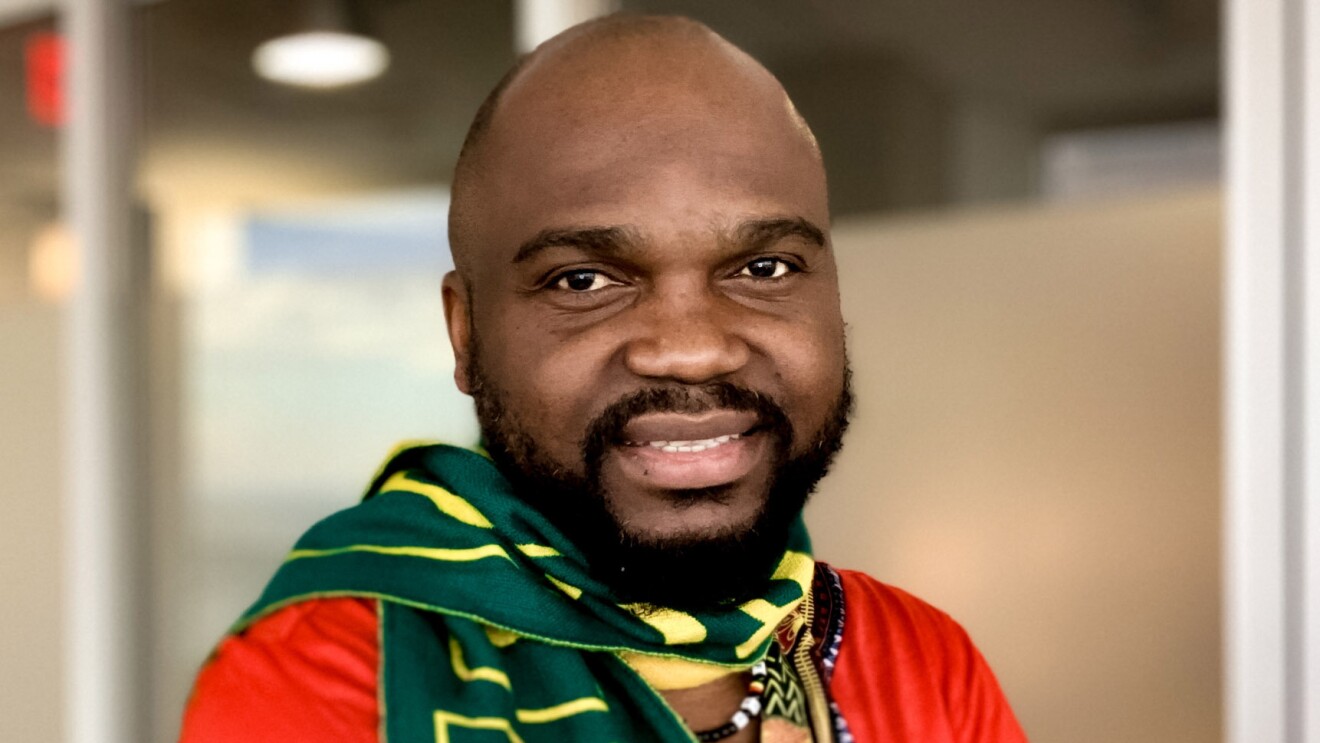An image of a man smiling for a headshot photo. He is wearing a bright red shirt and a green and yellow scarf.