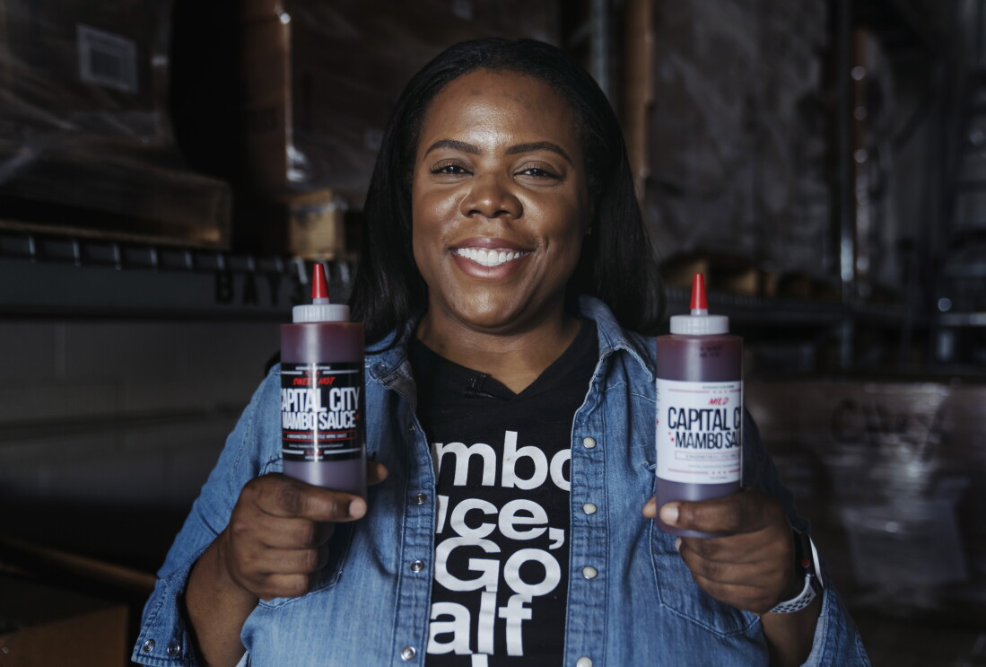 Arsha Jones holds up the two different flavors of sauces she makes and smiles for the camera.