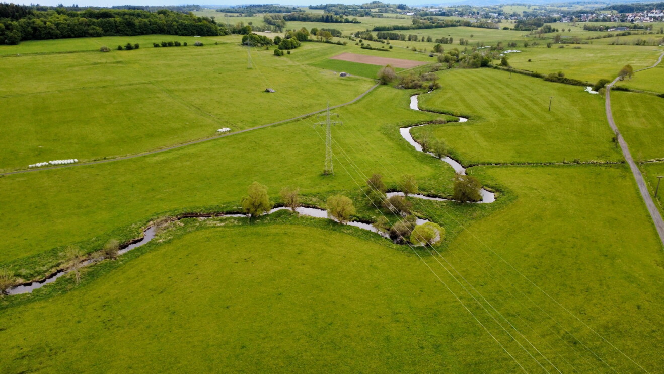Lush countryside with a meandering river and power lines overhead