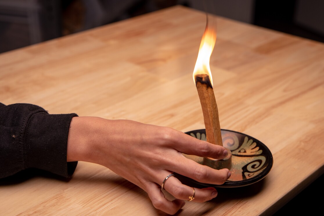 Close-up photograph of a hand placing a piece of burning wood in a ceramic holder.