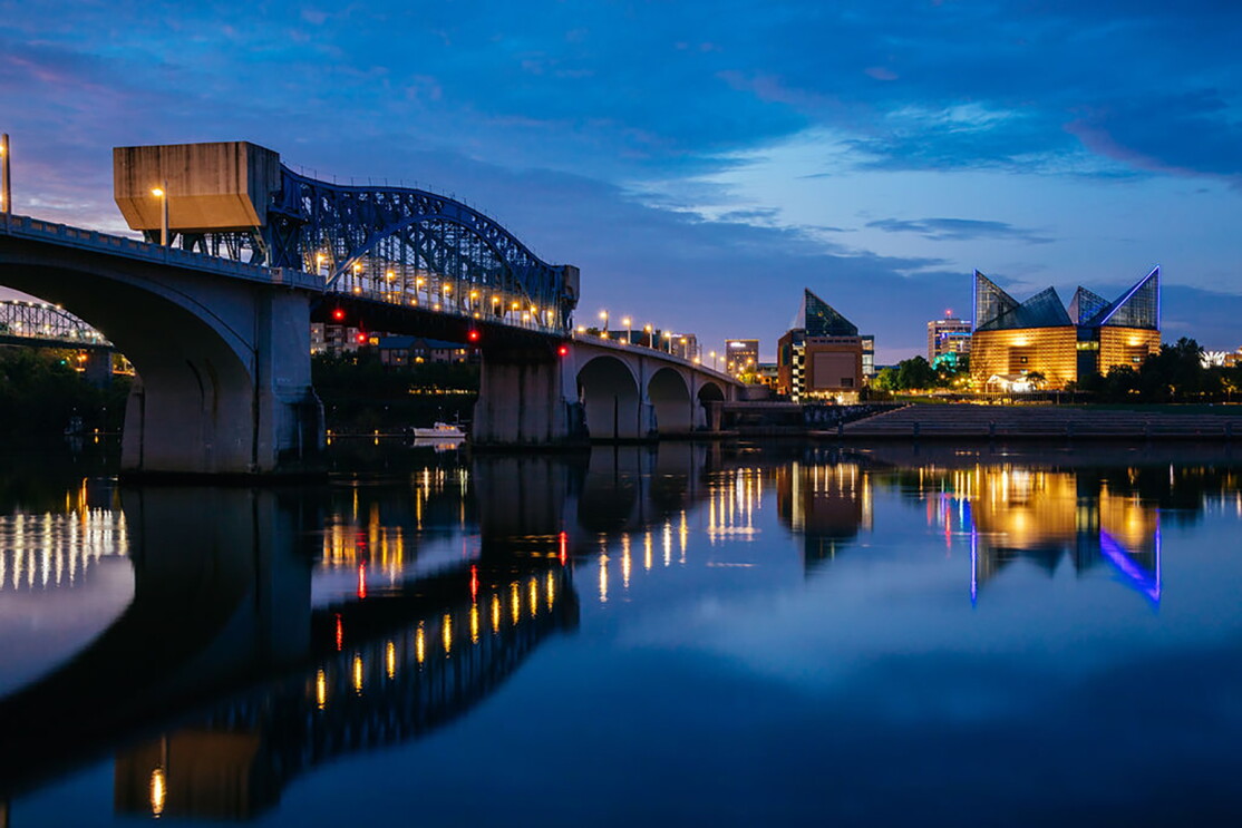 The Tennessee river at night, with a bridge stretching along it's width. In the foreground, Chattanooga buildings are lit up.