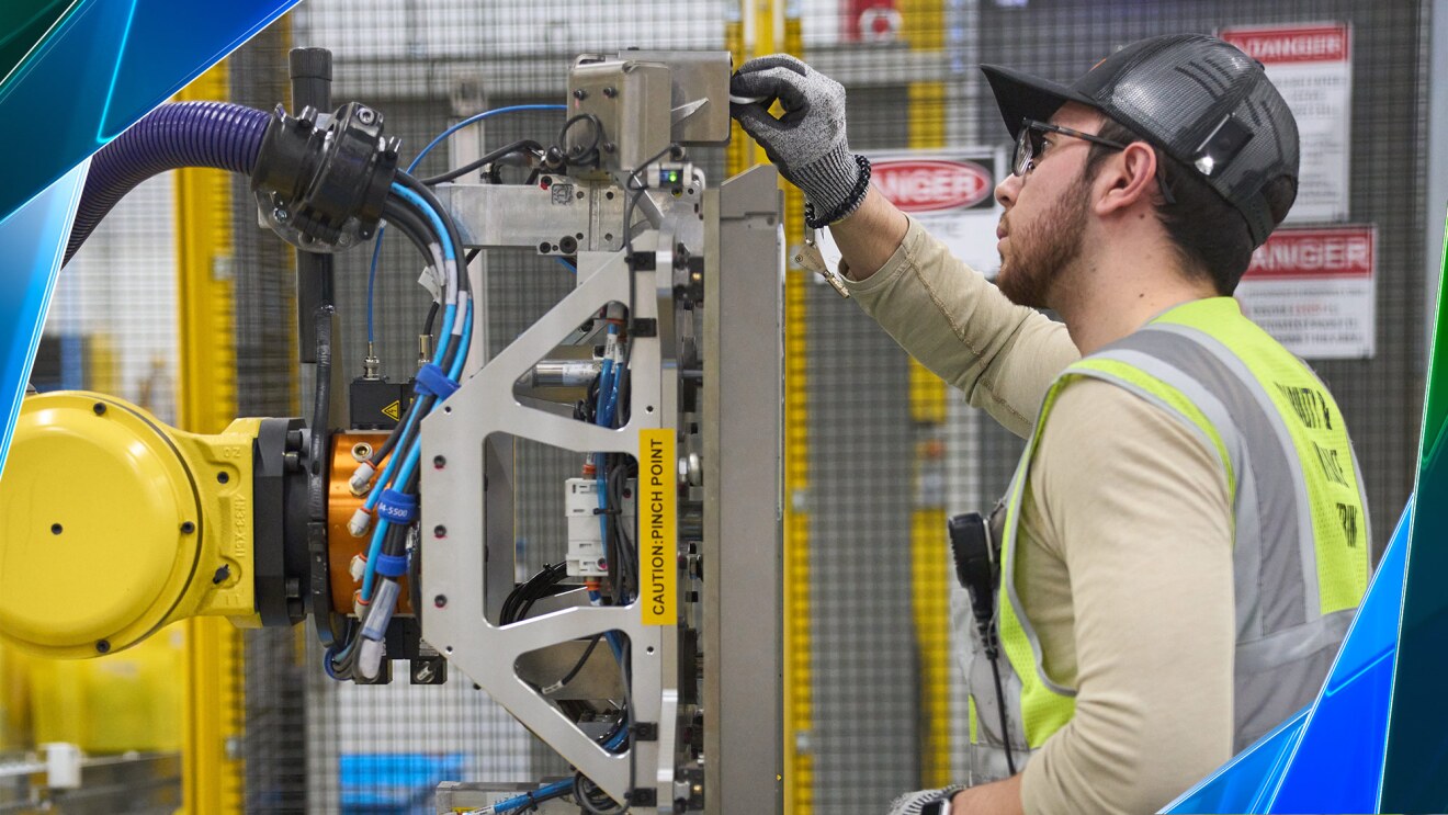 Un empleado de Amazon lleva un chaleco de seguridad amarillo y trabaja con un robot.