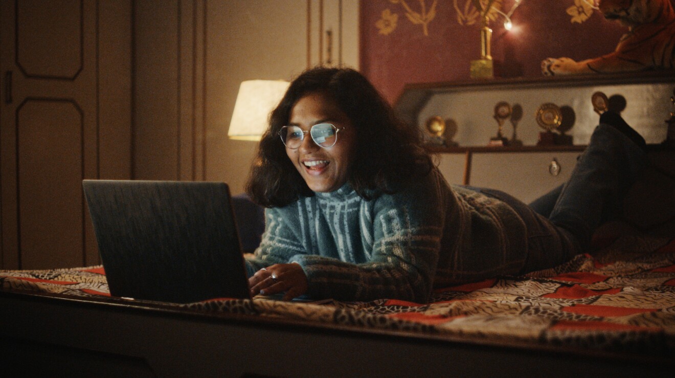 A photo of Vani Agarwal laying on her bed, using her laptop device.