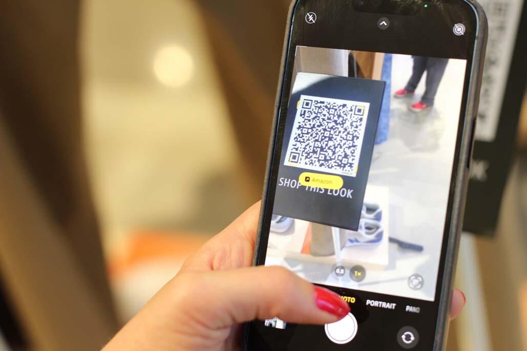 A hand is holding a phone. On the screen, the camera is scanning a QR code and there is a pop up for an Amazon link.