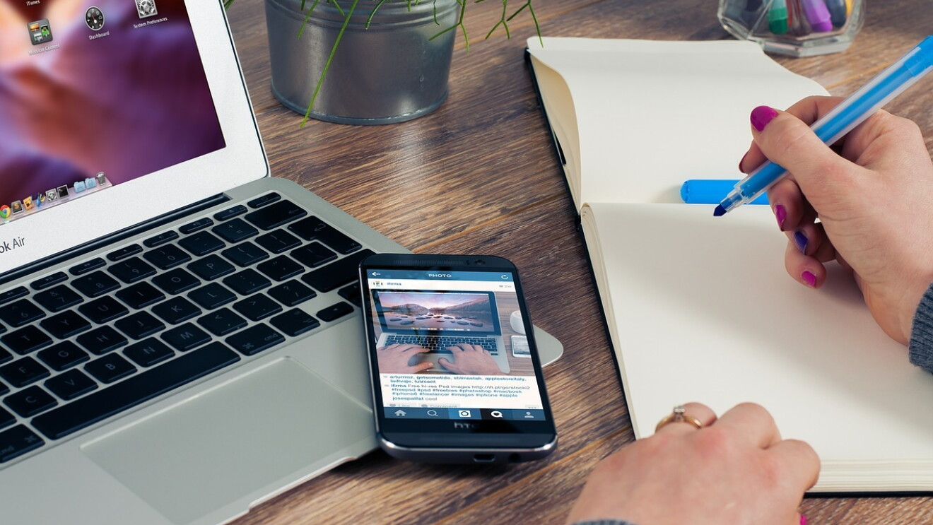Picture of a laptop and a notepad with a lady's hand holding a pen against a notepad