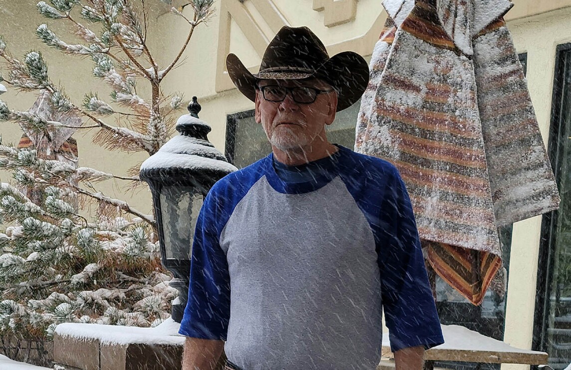An image of a man standing for a photo outside in the snow wearing a cowboy hat.