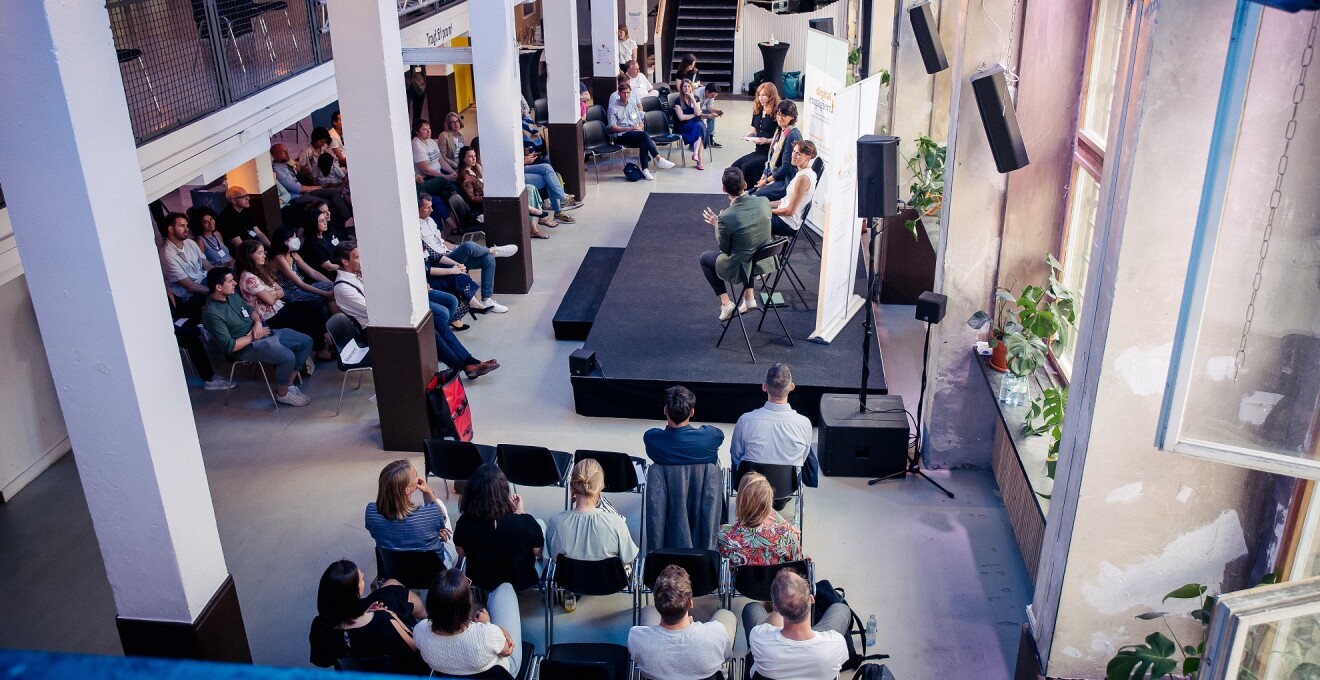 Gäste sitzen vor einer Bühne, auf der sich Personen in einem Panel der digital.engagiert-Abschlussveranstaltung austauschen.