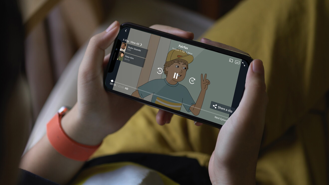 A girl holding a smartphone horizontal while sitting with her legs crossed on armchair in living room.