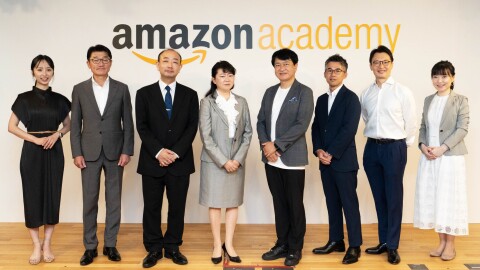 フォーマルウェアを着ている女性3人と男性5人が白い壁の前に立って並んでいる。背後にAmazon Academyの文字