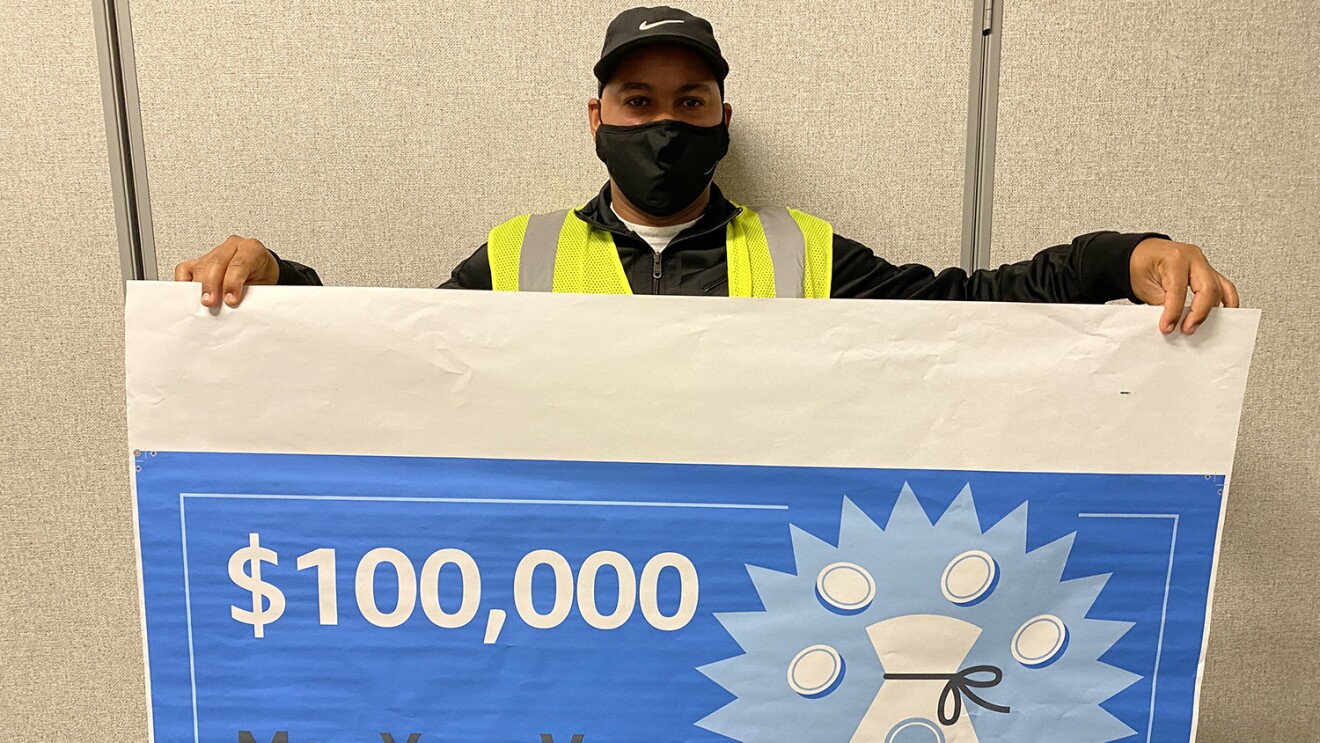 An image of a man holding a large check that says "$10,000 Max Your Vax WINNER"