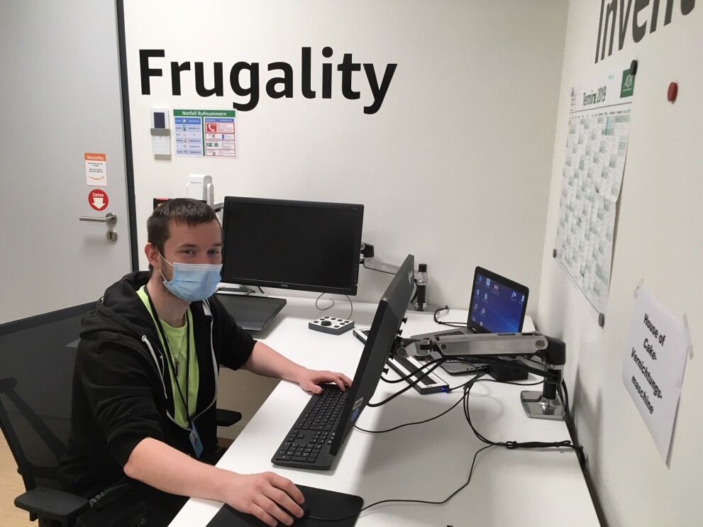 Ein junger Mann mit Mundschutz an einem PC-Arbeitsplatz
