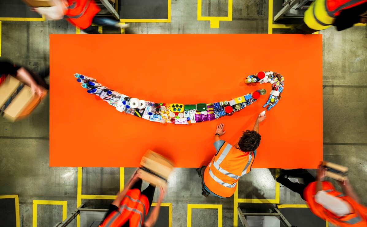 Worker arranging Amazon smile logo made of products on orange background