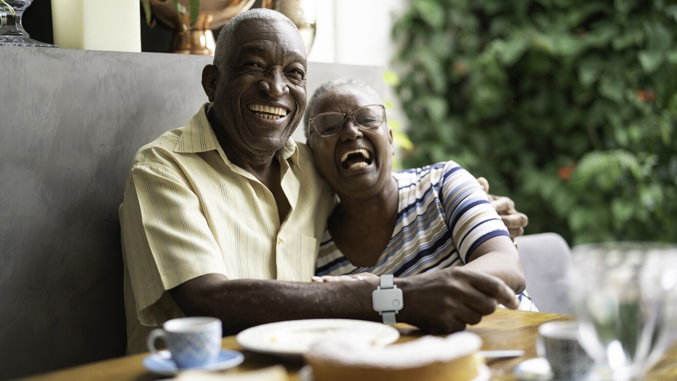 An image of a senior couple sitting in a booth at a table hugging each other and smiling.