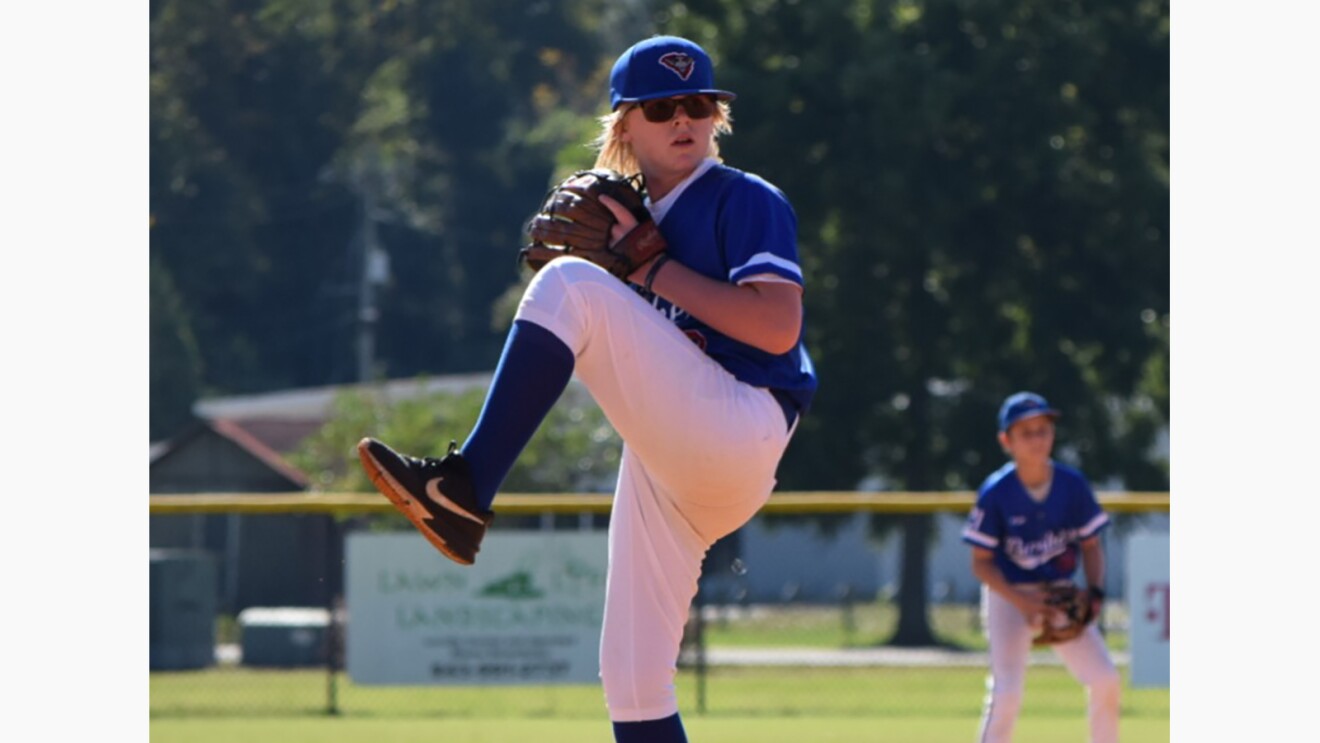 Gavin, preparing to pitch a baseball. He is wearing a baseball uniform and sunglasses.