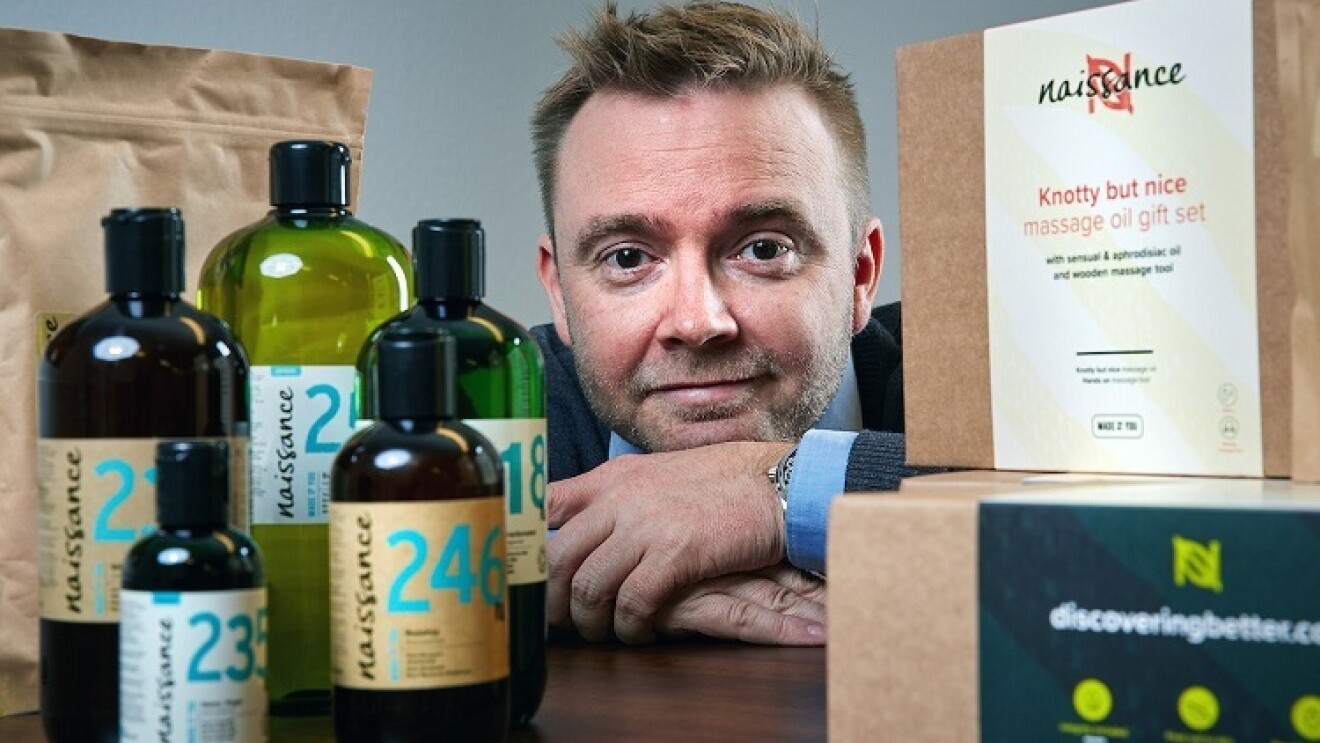 Man dressed in a suit, positioned behind bottles and cardboard boxes