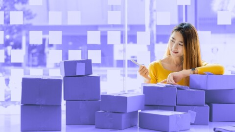 紫色で統一された室内に、紫色のパッケージが10点ほど並ベラれている。その後ろに黄色い服を着た女性がスマートフォンを見ている