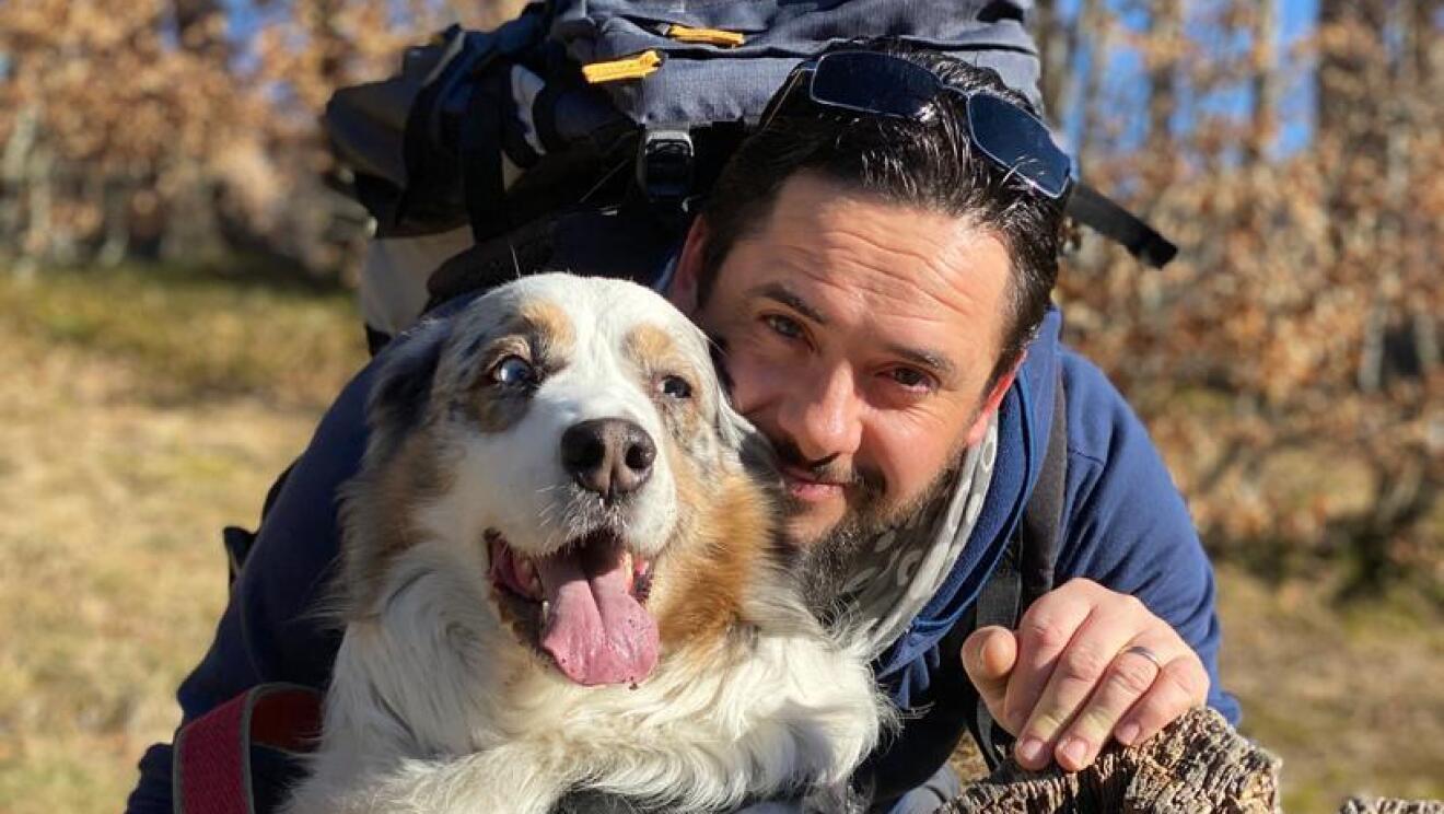 Foto di Matteo Alberti in un ambiente naturale con il suo cane. Posano sul tronco di un albero.