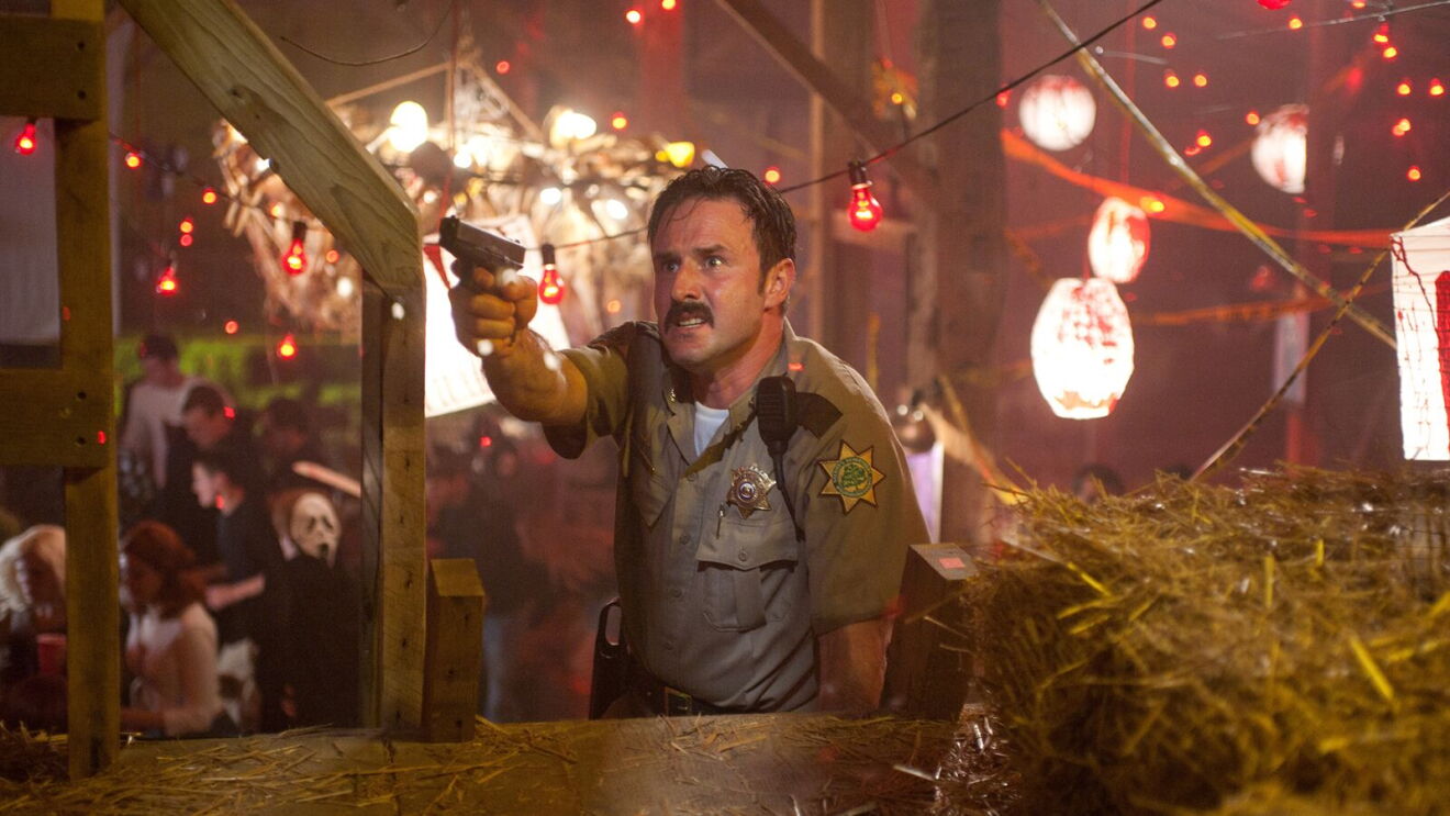 David Arquette as a sheriff aims pistol amid festive barn party lights in Scream 4