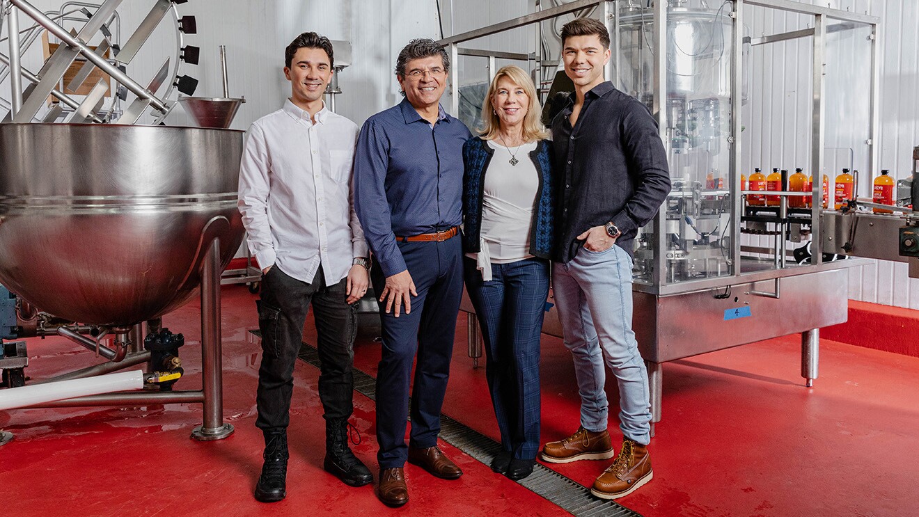 A photo of the family owners of Lucy's Inc. standing in in a factory. There are bottles of apple cider vinegar on a conveyor belt behind them.