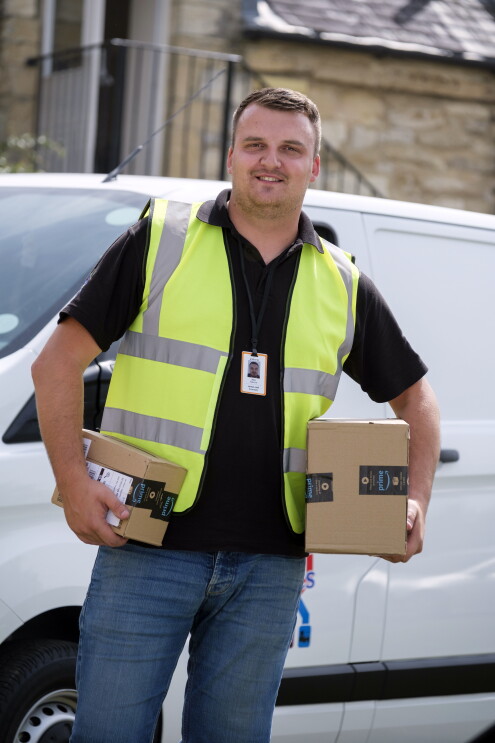 JMHC delivery driver holding Amazon packages in front of a delivery lorry