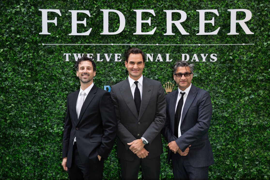 Three men in black suits in front of a grass background