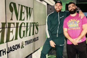 Travis and Jason Kelce standing beside 'New Heights' podcast promotional display