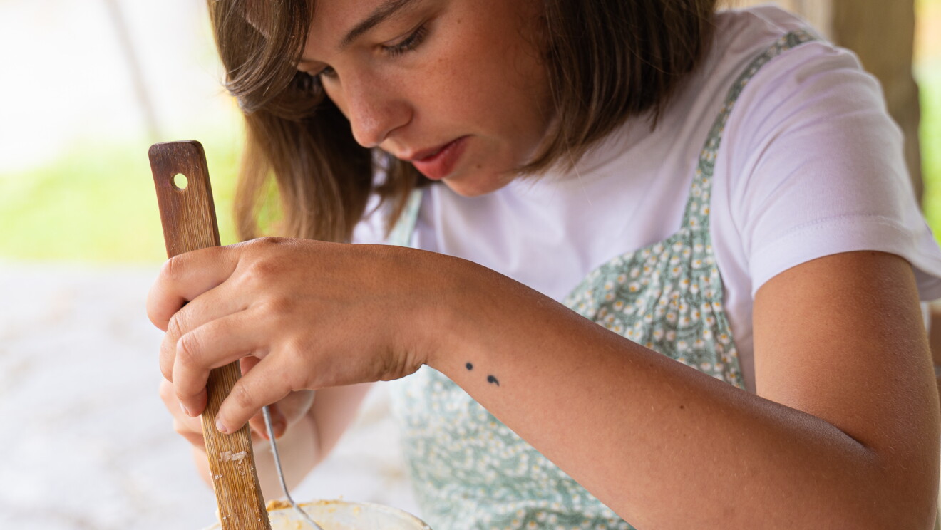 María Gómez Iribarnegaray mezclando los productos naturales para crear un jabón sólido.  María mezclando en la terraza de casa de su abuela en Villasana de Mena. En un recipiendo de cristal y encima de una table de madera, en una mano una pala de madera u en la otra de cristal. 