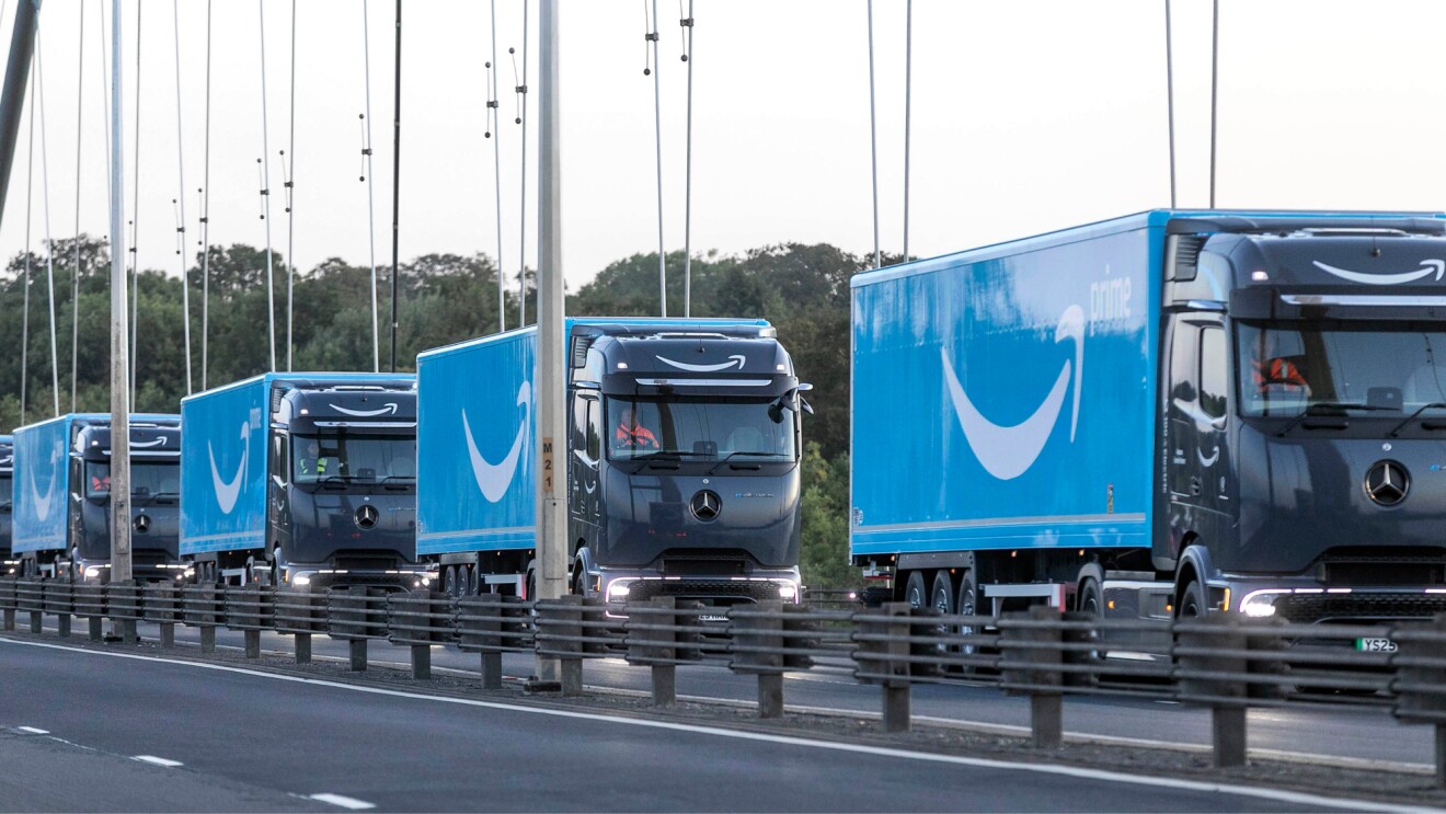 Convoy of blue Amazon trucks driving down a motorway