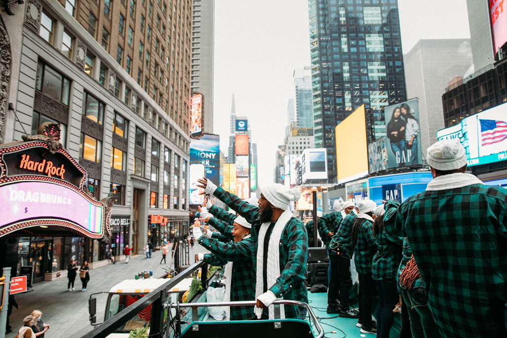 An image of the Harlem Gospel Choir on top of a green double-decker bus singing to crowds in New York.