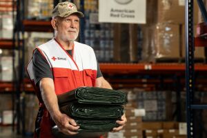 American Red Cross volunteer carrying green tarps in warehouse