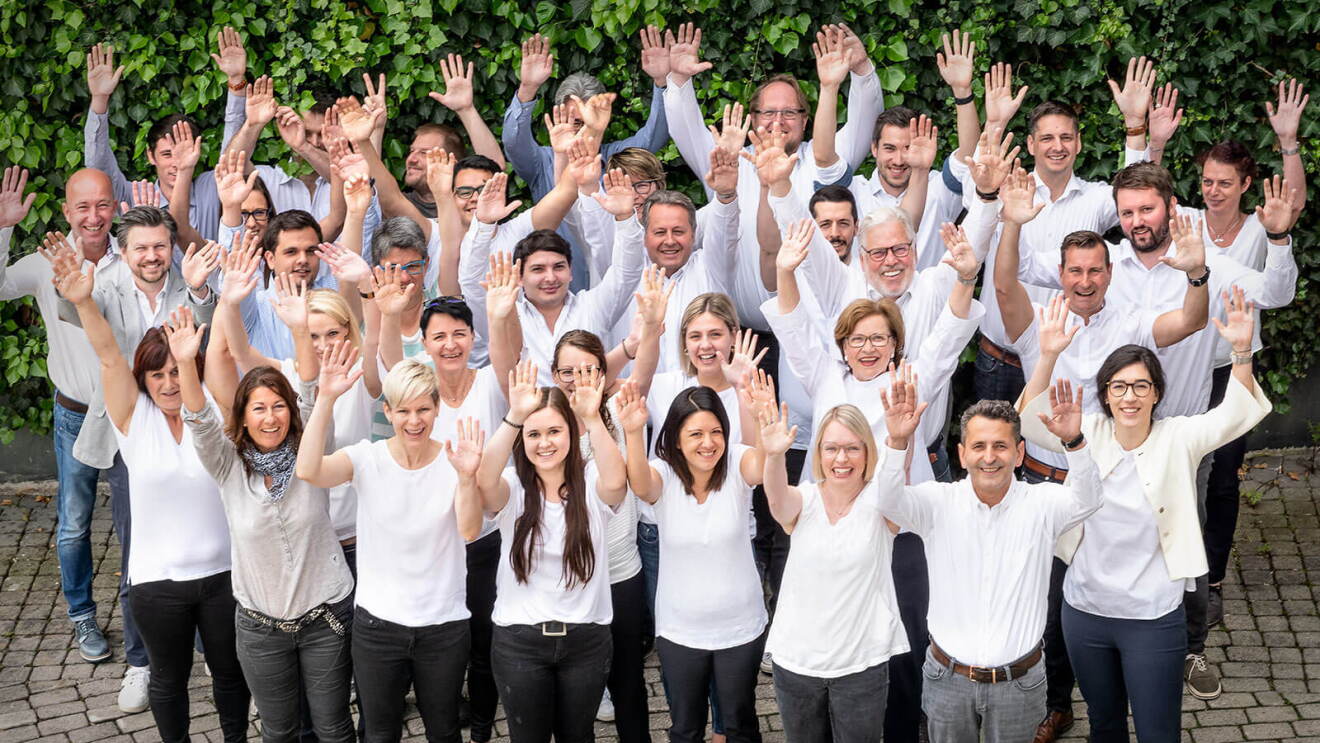 Das Team des Autozubehörproduzenten Walser aus Hohenems in Österreich steht in weißen T-Shirts bekleidet mit hoch gestreckten Armen auf einem begrünten Innenhof.