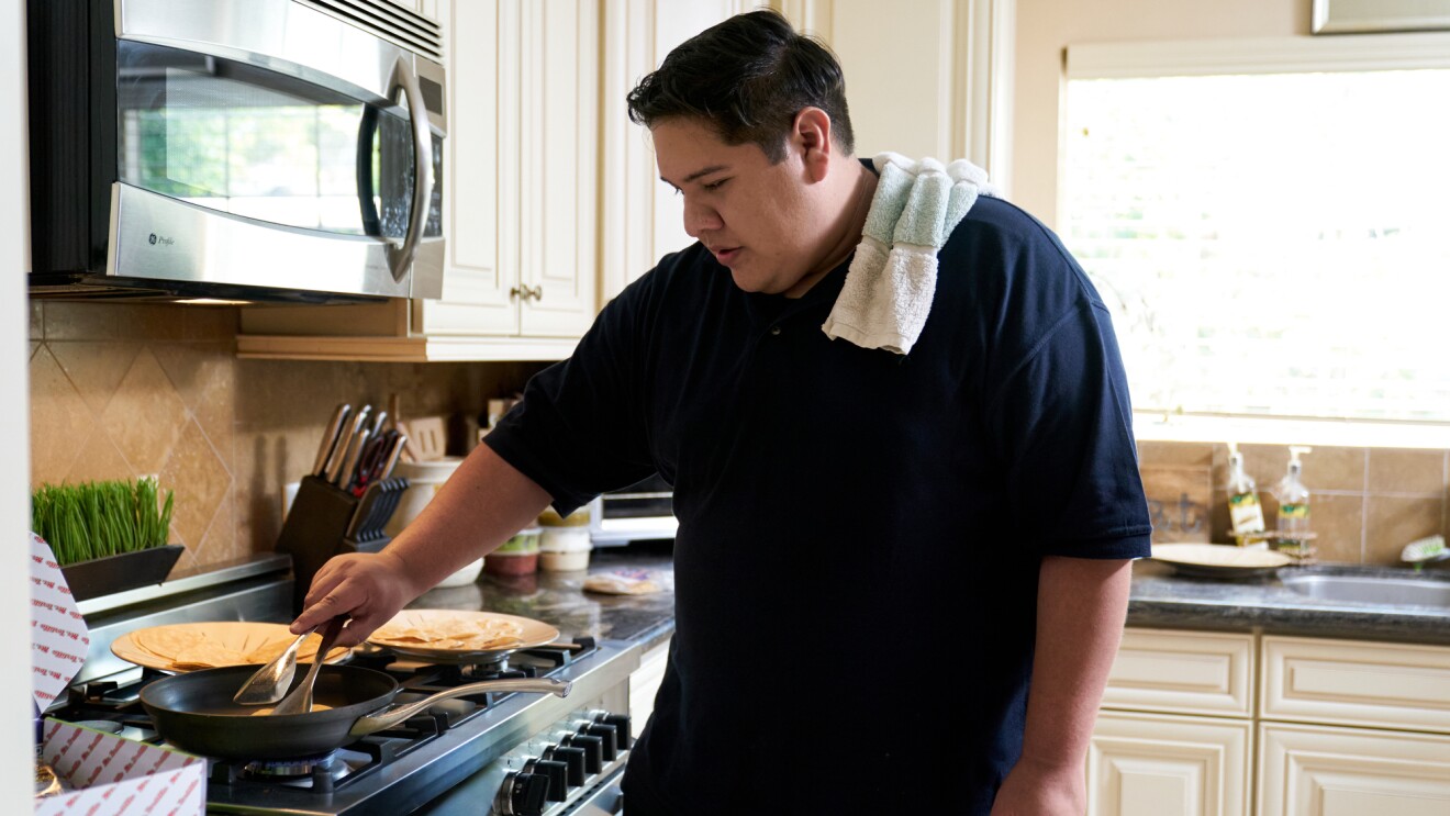 A man holding tongs cooks tortillas on a skillet.