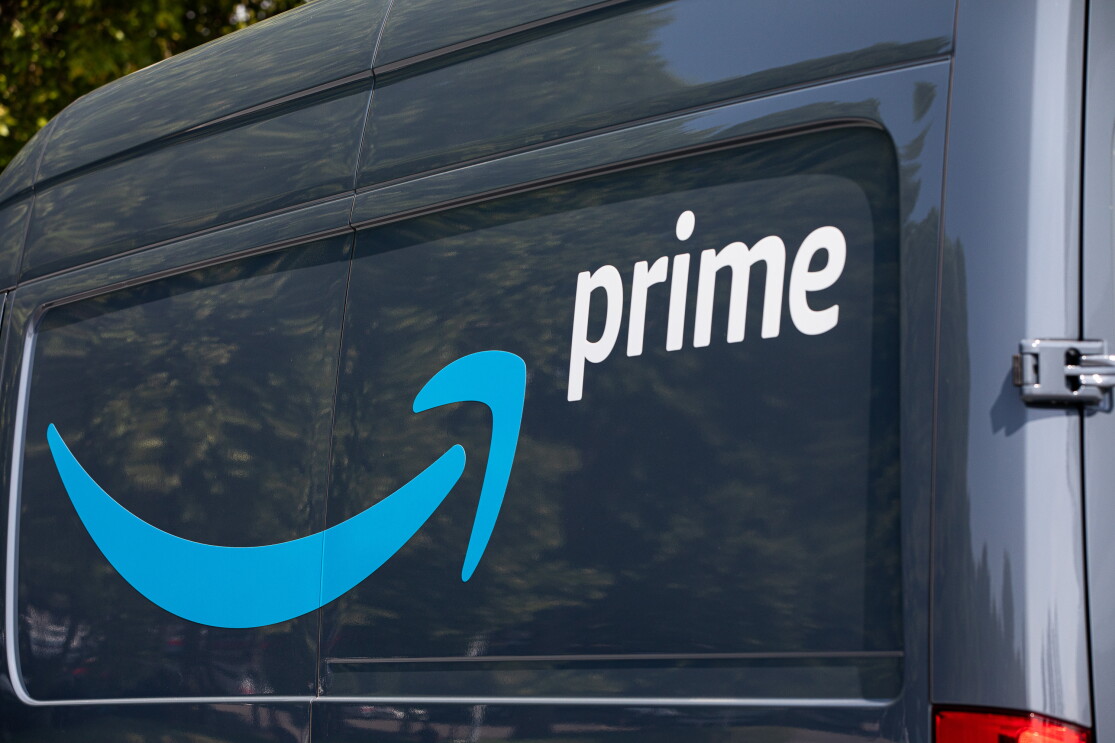 Parte trasera de una furgoneta de reparto. Letras Prime en blanco y la sonrisa de Amazon en azul. 