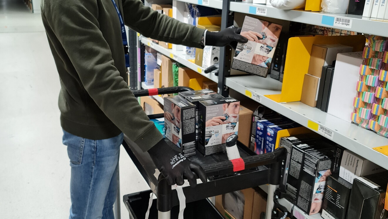 Amazon employee, Raimonds Duboks adding products to a shelf whilst on a ladder and wearing a mask