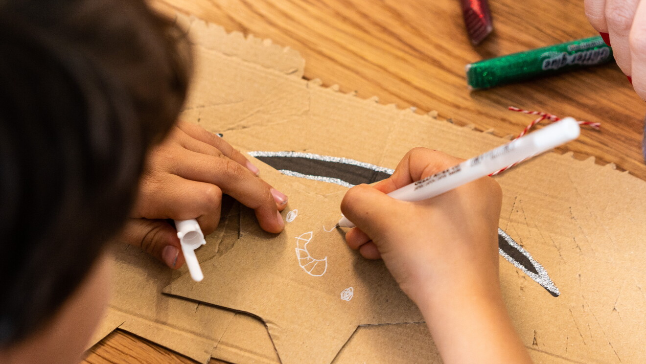 Diego, el hijo de marta y Fernando, dibujando una estrella para el árbol de Navidad. Primer plano de las manos de Diego. En la derecha un color blanco que ilustra la estrella. La estrella es de carta de cartón de Amazon. En la mano izquierda sujeta el tapón.  