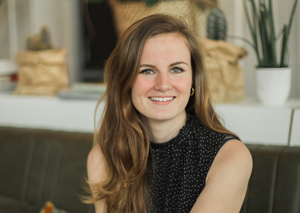 A headshot image of a woman smiling for a photo while seated on a bench in a dining room.