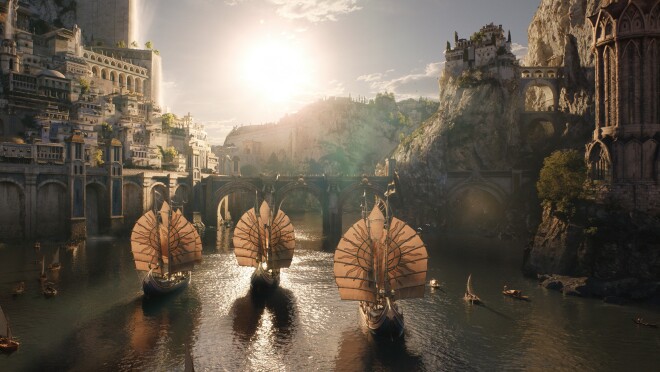 A scene from the Lord of the Rings: The Rings of Power. Ships with circular sails move through a bay. There is a bridge and a city on the hill surrounding the bay.