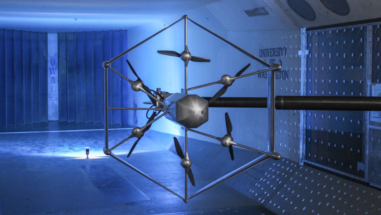 L'immagine mostra il rendering di un drone Amazon, di forma esagonale, con sei eliche, all'interno di un laboratorio. 