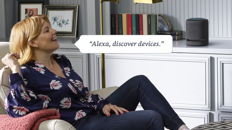 An image of a woman sitting on a chair in a living room speaking to an Amazon Echo device. There is a text box that reads "Alexa, discover devices."