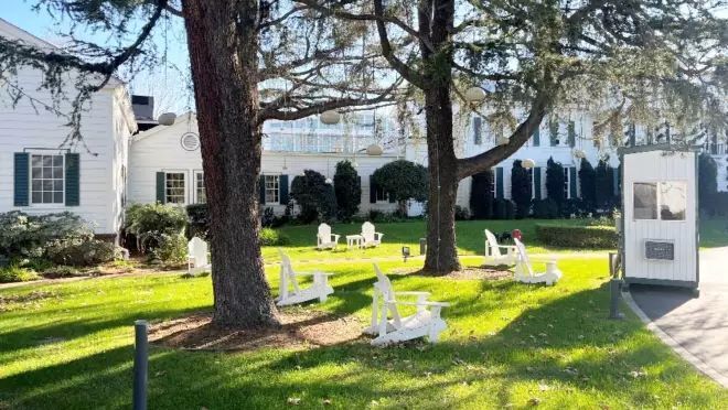 広大な庭園に数台の白い椅子が置かれている。その庭園は白いレトロな建物に囲まれています。