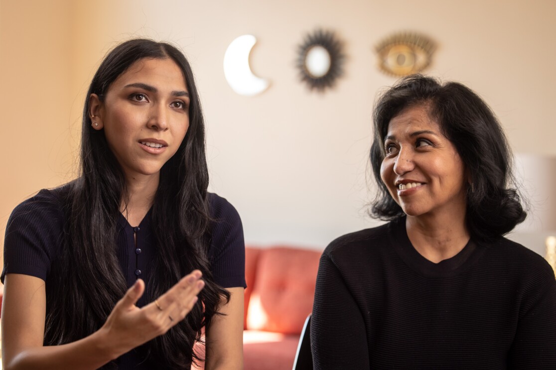 A woman speaks while another looks on and smiles.