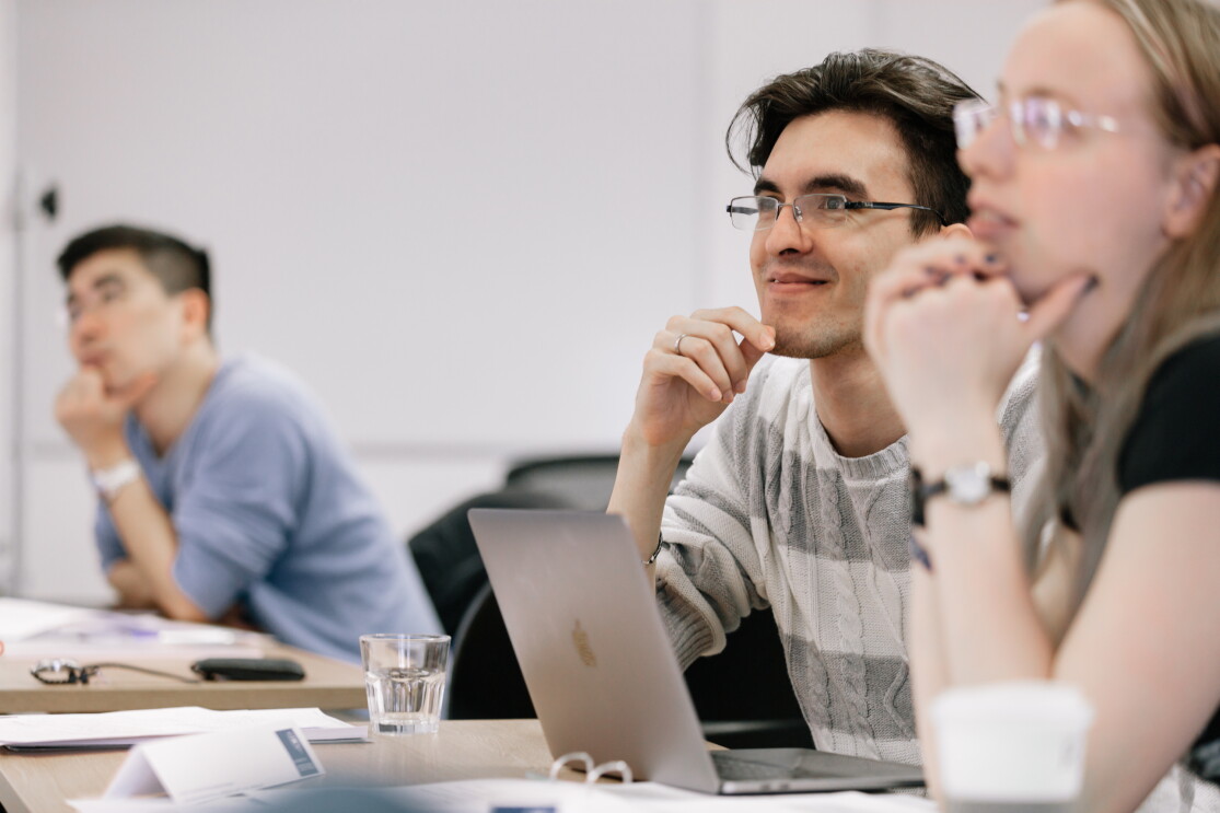 Students at the University of Oxford sitting in a lecture, they are sitting at their desks with their laptops, notes and drinks on the table. 