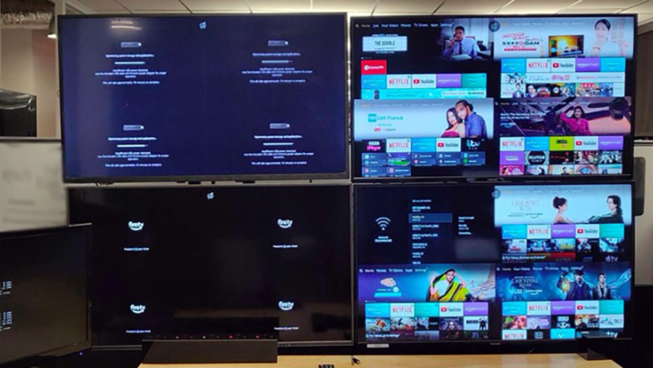 4 monitors in a work space, with a row of remotes and keyboard in front of them.