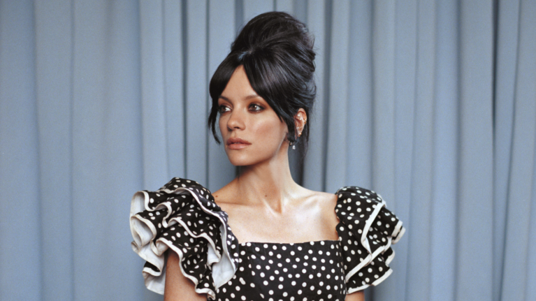 Lily Allen poses in a black and white polka dot dress against a blue background for Prime Video.