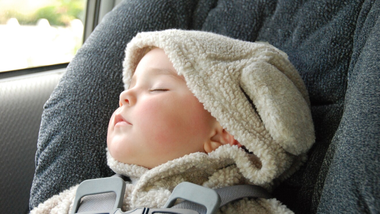 一个婴儿穿着连帽上衣和耳朵在汽车座椅上睡着了