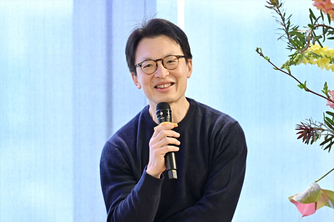 メガネをかけている男性がマイクを持って微笑んでいる