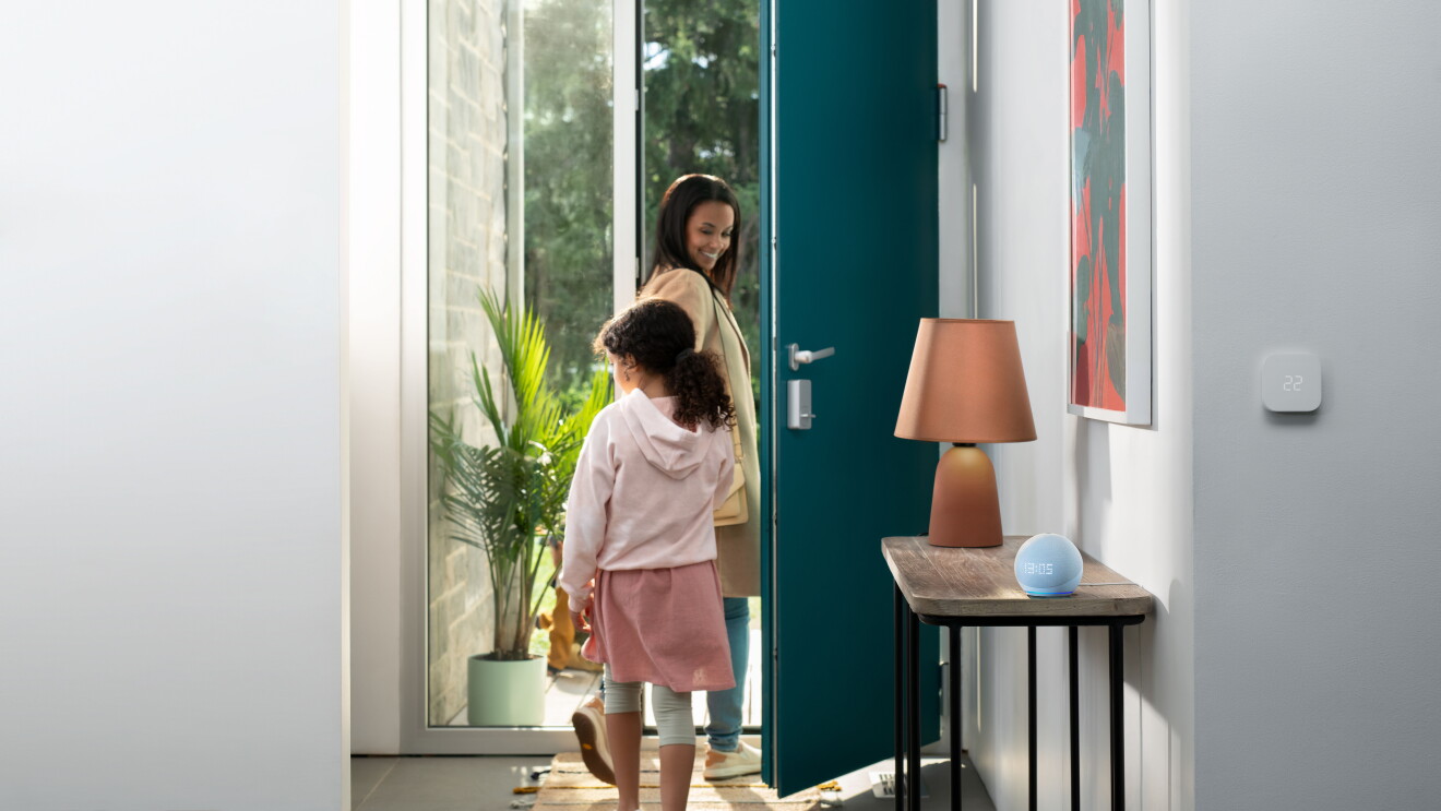 Una imagen de una mamá y su hija saliendo por la puerta de su casa. Un dispositivo Echo Dot se encuentra en la mesa al lado de la puerta.