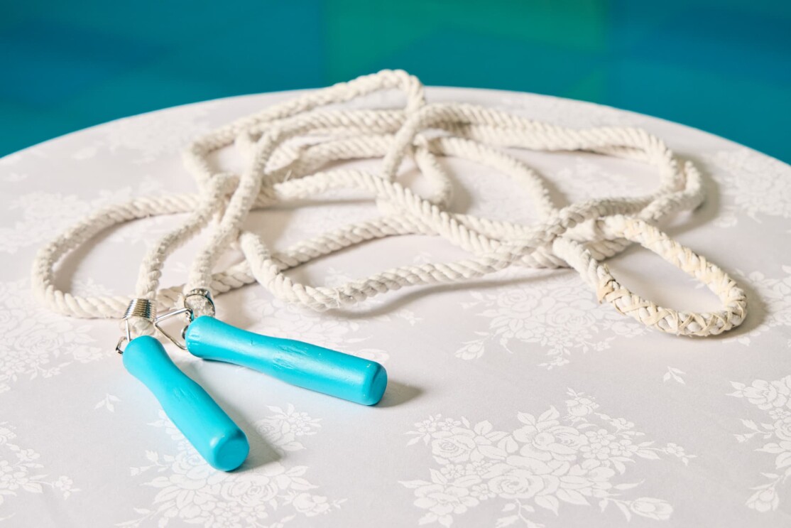 白いバラ模様のテーブルクロスがかかった丸テーブルの上に1本の縄跳びが置かれている。縄部分は白いローブ、持ち手部分は水色