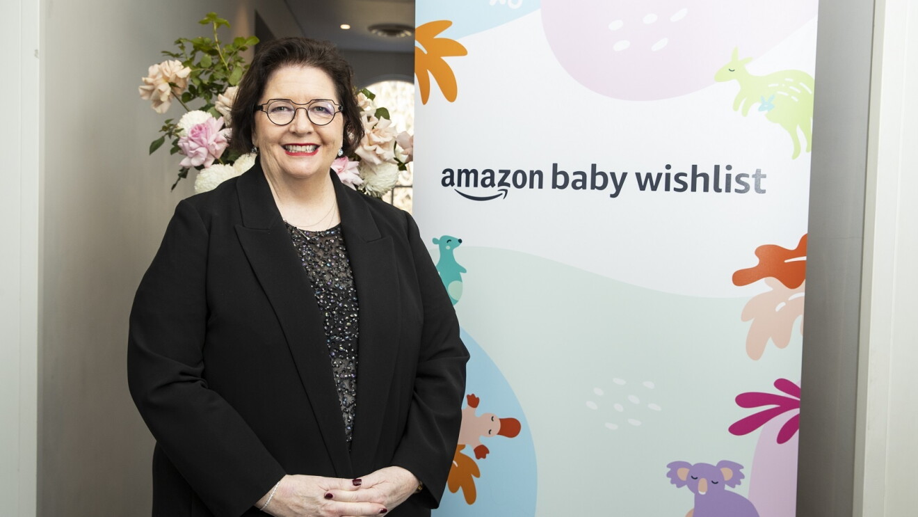 An image of a woman smiling in front of a sign that says "Amazon baby wishlist" with flowers around it.