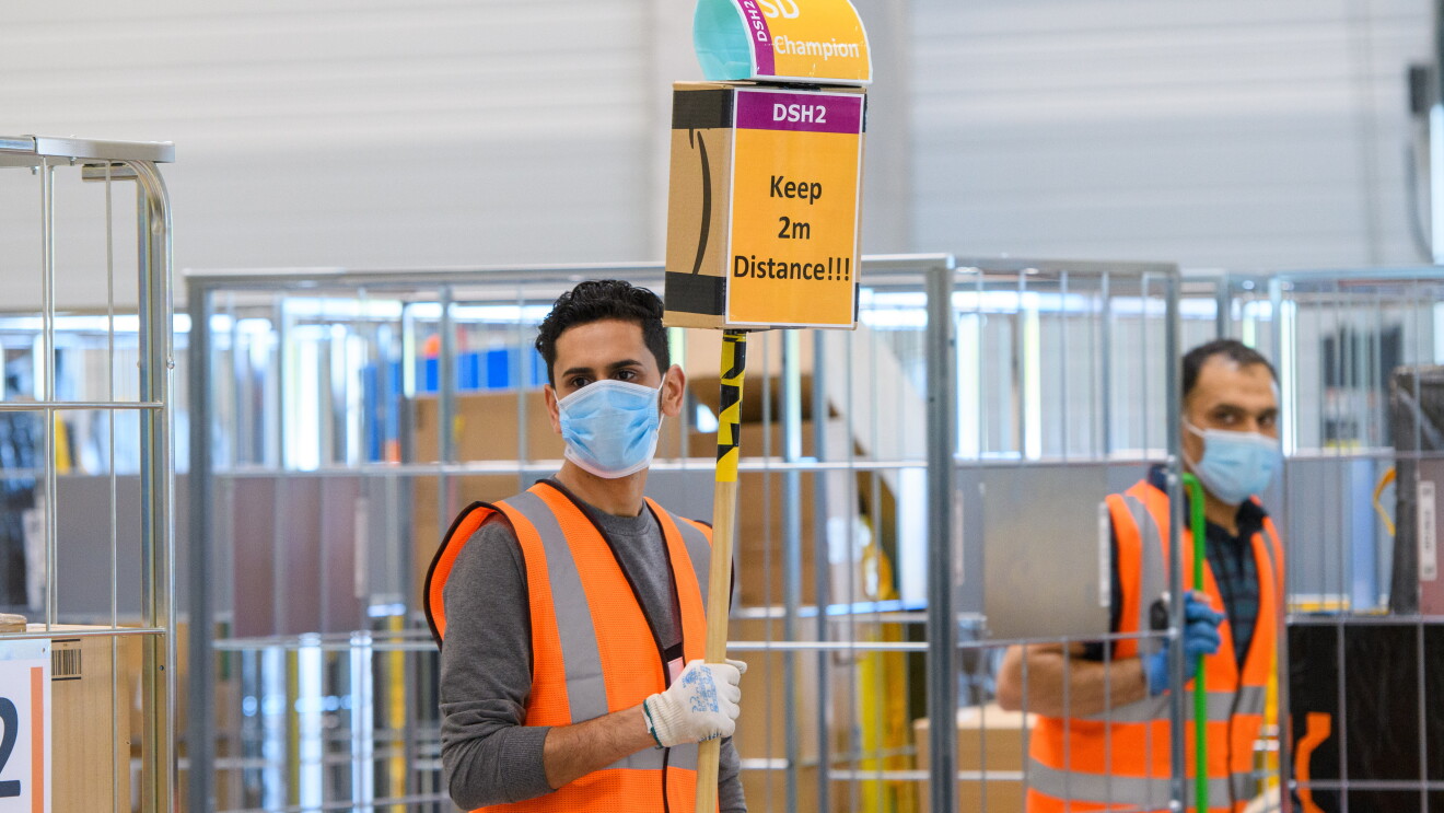 Ein Mitarbeiter in Sicherheitsweste mit einem Schild: "Keep 2 m Distance!"